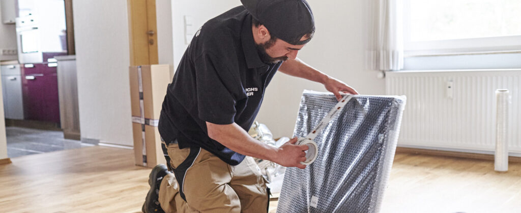 Derichsweiler Mitarbeiter klebt sorgfältig Luftpolsterfolie um einen gerahmten Gegenstand.