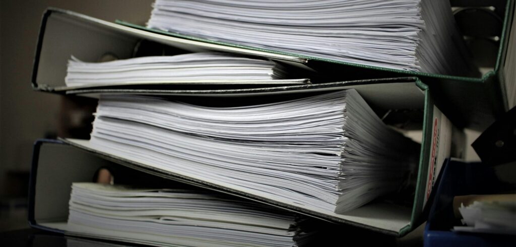 Three thick binders filled with large stacks of paper are piled on top of each other.