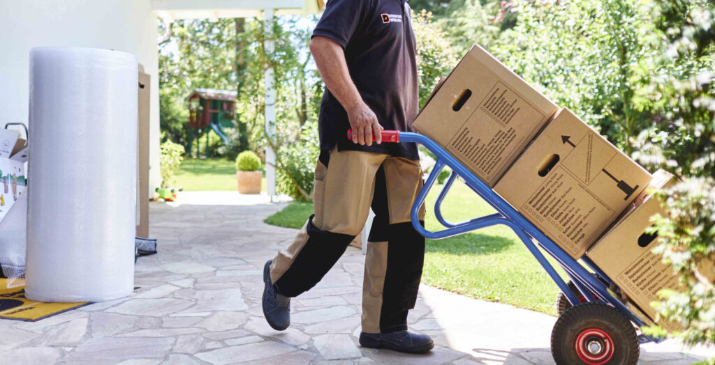 Derichsweiler Mitarbeiter transportiert Kartons auf einem Handwagen durch den Garten.