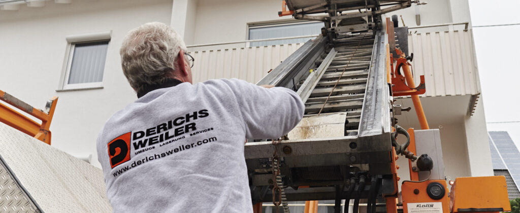 Derichsweiler Mitarbeiter bedient einen beweglichen Lift, der an einem weißen Haus positioniert ist.