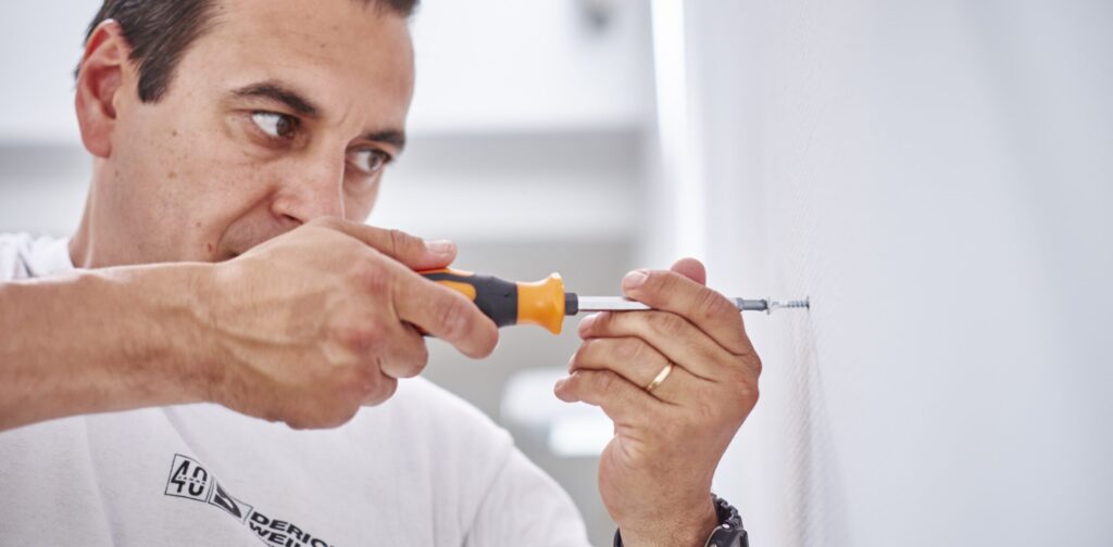 Unser Mitarbeiter dreht mit einem Schraubenzieher konzentriert eine Schraube in eine Wand.