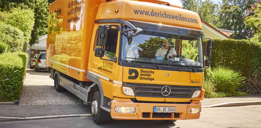 Orangefarbener Umzugswagen mit dem Derichsweiler Logo, geparkt in einer Vorstadt-Einfahrt.
